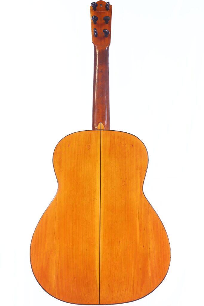 A imagem mostra o fundo de uma guitarra clássica Domingo Esteso 1934 com uma superfície de madeira natural, uma costura central vertical e cravelhas pretas no cabeçote contra um fundo branco liso.