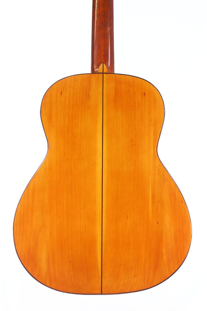 Um close-up da parte de trás do violão clássico Domingo Esteso 1934 destaca sua madeira lisa e polida e uma linha escura central que divide o corpo contra um fundo branco.