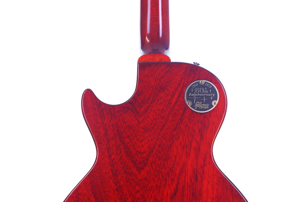 The Back Of A Red Gibson Les Paul 1960 60Th Vos Anniversary Electric Guitar With Visible Wood Grain And A Circular Metal Plate Near The Top Reading &Quot;60Th Anniversary&Quot; And &Quot;Gibson Custom,&Quot; Set Against A White Background.