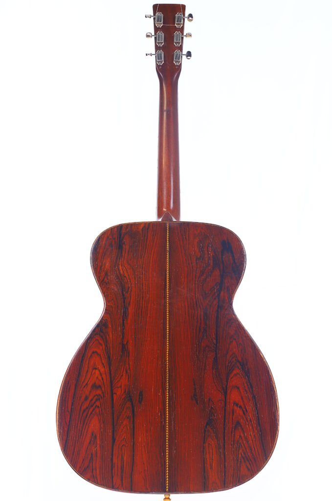 The Back View Of The Martin 000-21 1947 Acoustic Guitar Features Rich, Reddish Wood Grain With Dark Streaks And A Central Decorative Inlay, Set Against A White Background.