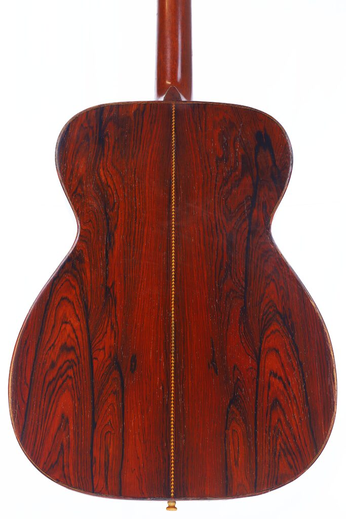 The Back Of A Martin 000-21 1947 Acoustic Guitar Features Glossy, Reddish-Brown Wood With Visible Dark Grain Patterns, Displayed Against A White Background.