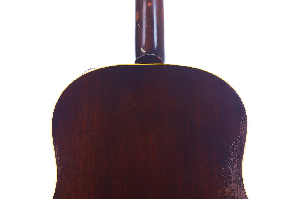 Close-Up Of The Back Of A Gibson J-45 1957 Acoustic Guitar, Featuring Its Dark Brown, Glossy Wood Body And Textured Finish, Shown Against A White Background With The Base Of The Neck Visible.