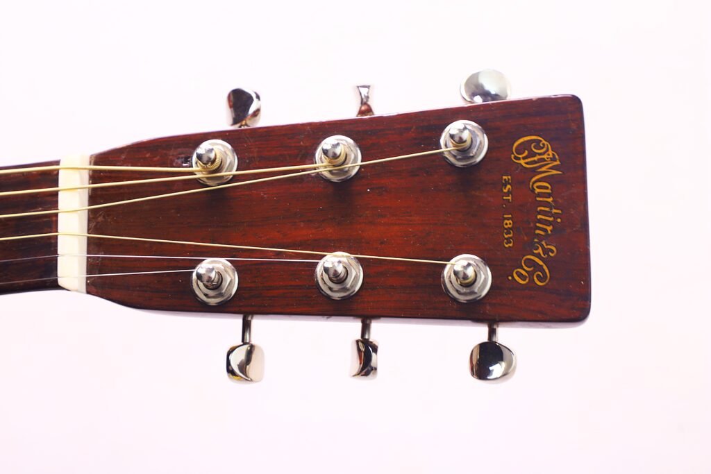 Close-Up Of The Headstock Of A Martin 00-18 1946 Acoustic Guitar With Six Tuning Pegs, Steel Strings, A Dark Wood Finish, And &Quot;Martin &Amp; Co. Est. 1833&Quot; In Gold Script On The Headstock.