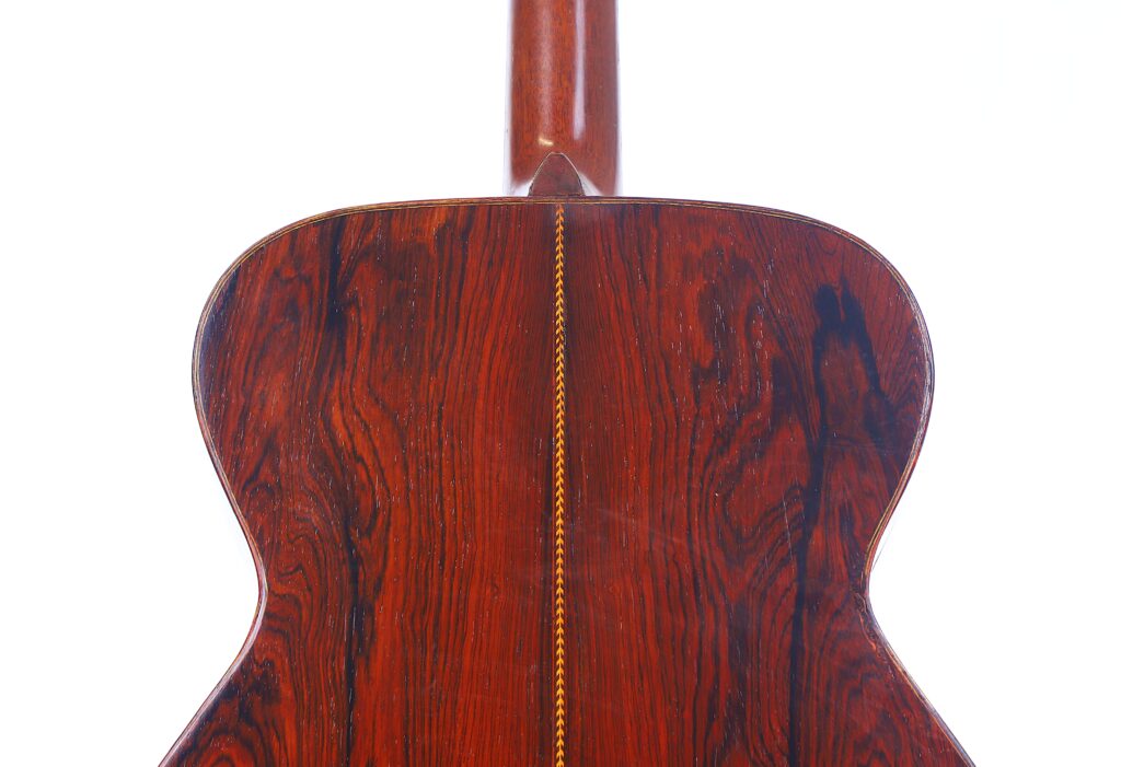 Close-Up Of The Back Of A Martin 000-21 1947 Acoustic Guitar, Featuring Rich Reddish-Brown Wood Grain And A Decorative Yellow Zigzag Inlay Running Vertically Down The Center.