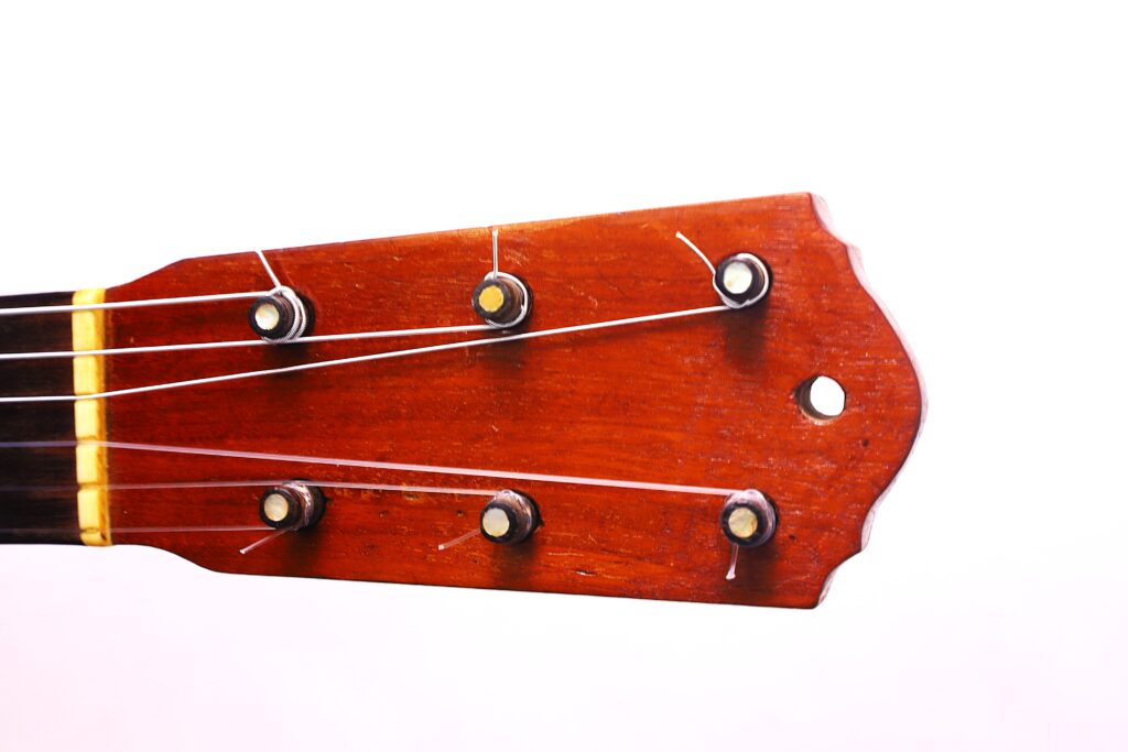 Grande plano do cabeçote de madeira da guitarra clássica Domingo Esteso 1934, com seis cravelhas e cordas, contra um fundo branco simples.