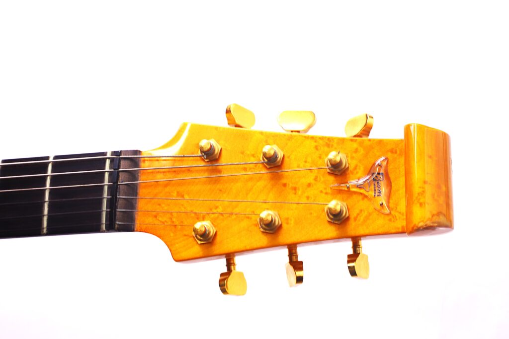 Close-Up Of The Burns Legend 1994 Electric Guitar’s Wooden Headstock With Six Tuning Pegs And Black Strings, Set Against A White Background.