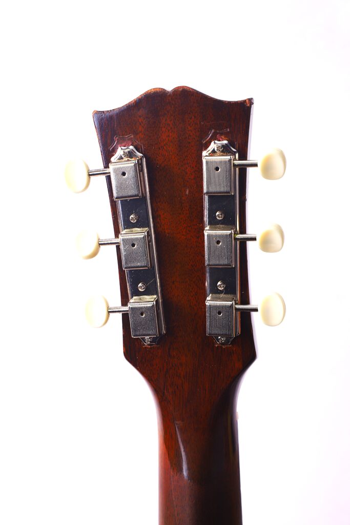 The Image Shows The Back Of A Gibson J-45 1957 Acoustic Guitar Headstock With Six White Tuning Pegs And Chrome Tuning Machines Against A Plain White Background.