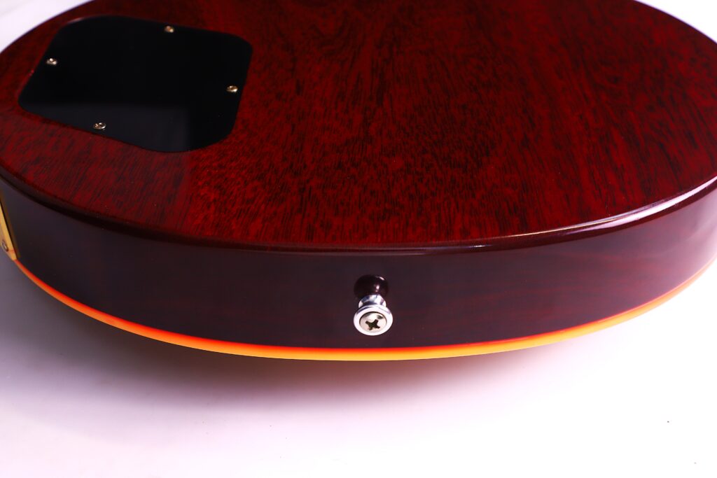 Close-Up Of The Back And Side Of A Dark Reddish-Brown Gibson Les Paul 1960 60Th Vos Anniversary Electric Guitar Body With A Black Plastic Cover Plate And Metal Strap Button Against A White Background.