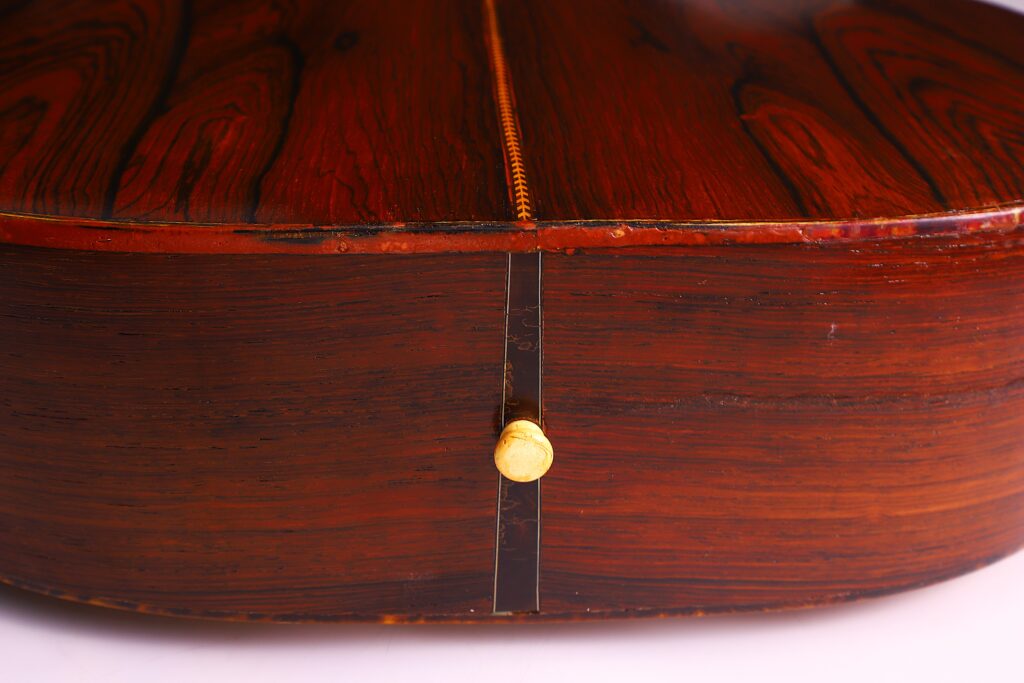 Close-Up Of The Back And Side Of A Martin 000-21 1947 Acoustic Guitar, Highlighting Its Rich Reddish-Brown Wood Grain, Decorative Center Seam, And Small Yellow Endpin At The Base.
