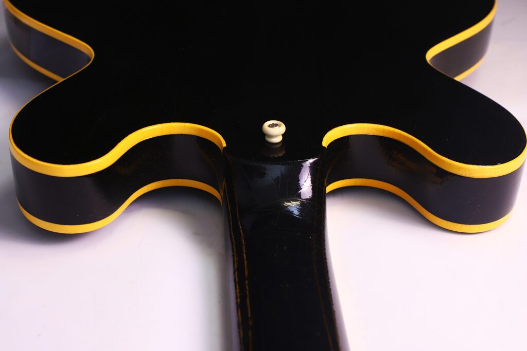 Nahaufnahme Der Rückseite Einer Schwarzen Gibson Es-335 Td Murphy Lab E-Gitarre Mit Gelber Zierleiste, Die Den Halsansatz Und Den Gurtknopf Vor Weißem Hintergrund Hervorhebt.