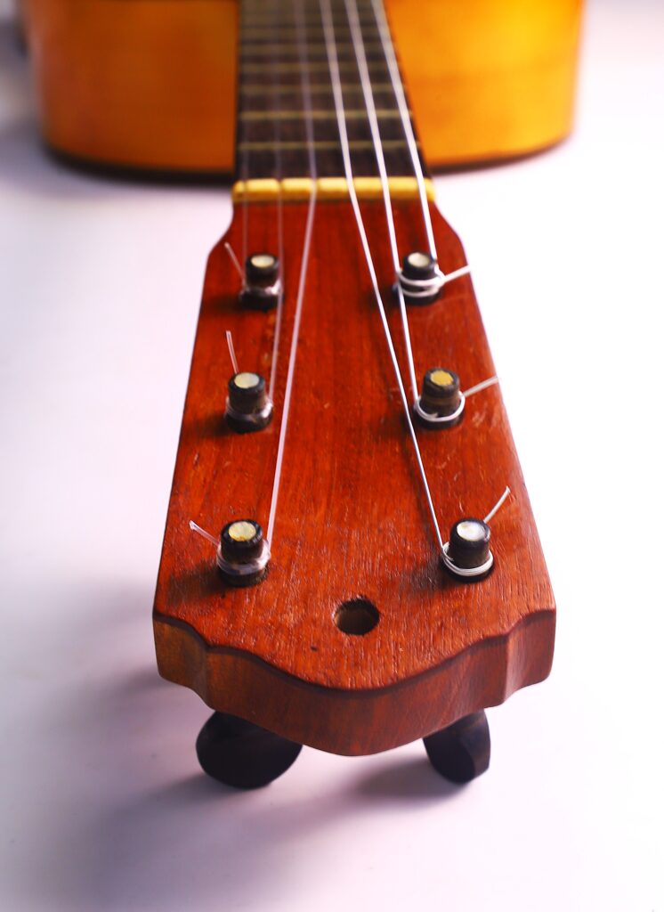 Grande plano do cabeçote de uma guitarra clássica Domingo Esteso 1934, mostrando as cravelhas e as cordas, com o braço e o corpo esbatidos numa superfície branca ao fundo.