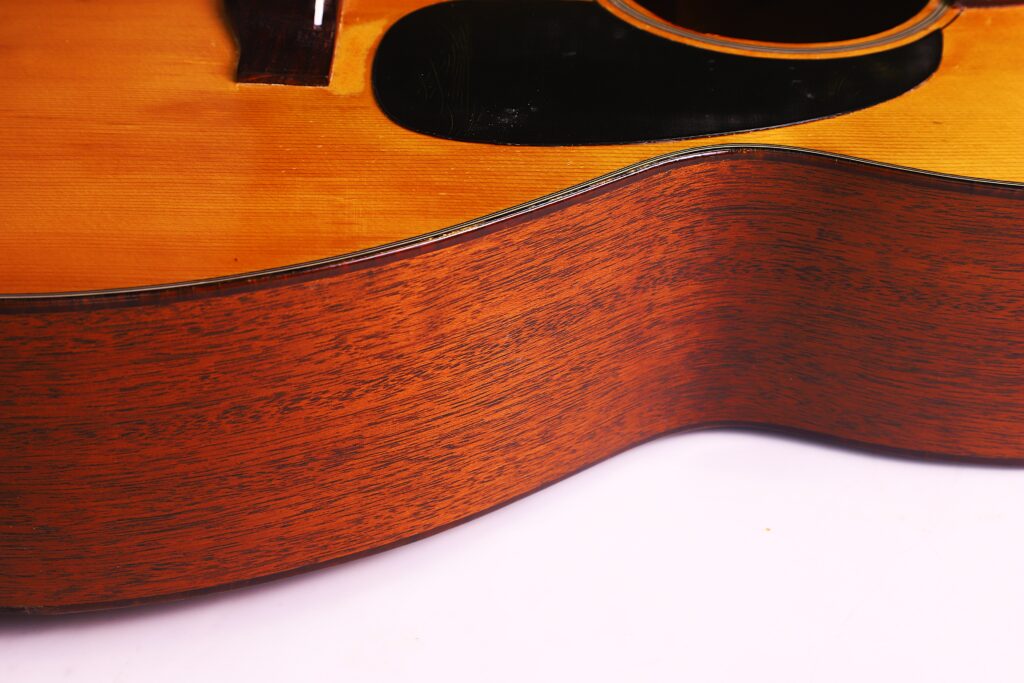 Close-Up Of The Side Of A Martin 00-18 1946 Acoustic Guitar, Highlighting Its Wood Grain And Smooth Finish. The Sound Hole And Pickguard Are Partially Visible At The Top, Set Against A White Background.