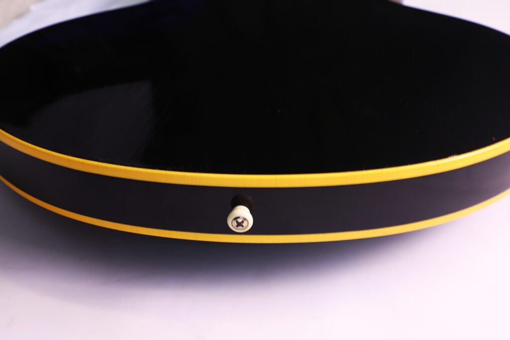 Nahaufnahme Der Unterkante Einer Schwarzen Gibson Es-335 Td Murphy Lab E-Gitarre Mit Gelber Zierleiste Und Einem Mittig Platzierten Gurtknopf Aus Metall, Auf Einer Weißen Oberfläche Liegend.