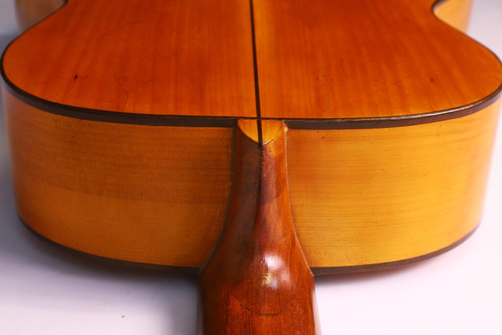 Grande plano da junta do braço de uma guitarra clássica Domingo Esteso 1934, destacando a junção do braço com o corpo, com grão de madeira visível e tons castanhos quentes.