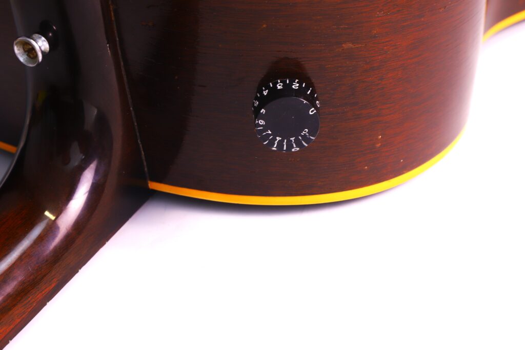 Close-Up Of A Gibson J-45 1957 Acoustic Guitar Body Highlighting A Black Volume Knob With White Numbers And A Yellow Accent Stripe, Set Against A White Background.