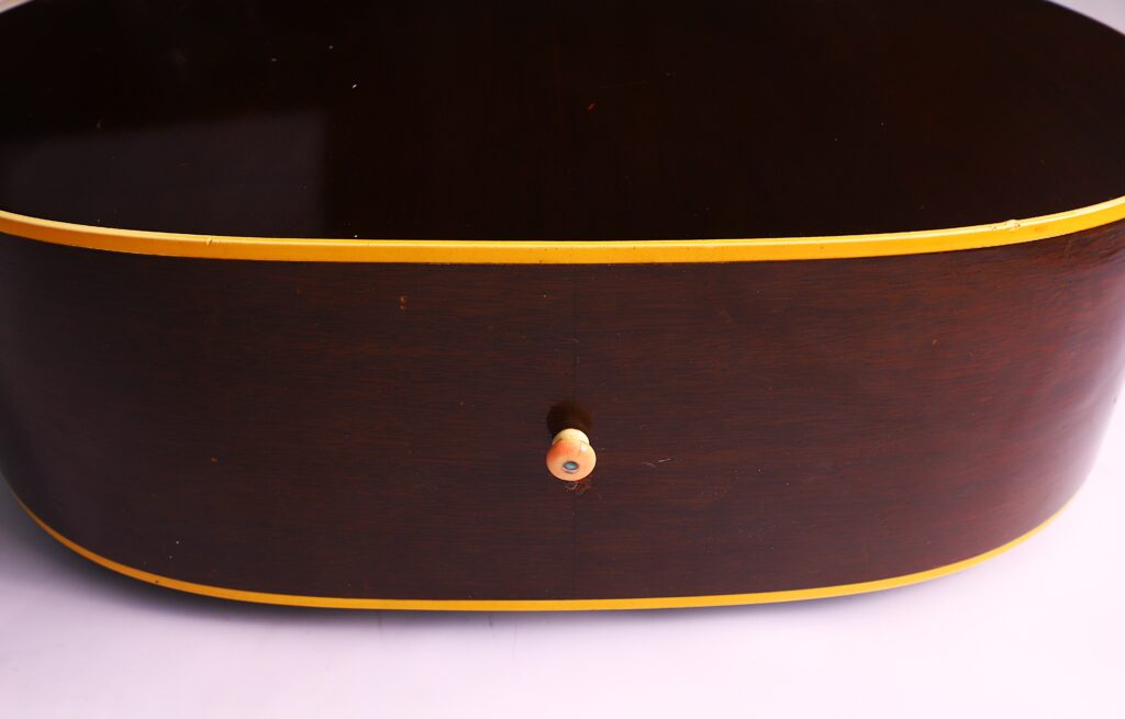 Close-Up Of The Gibson J-45 1957 Acoustic Guitar'S Side, Featuring Dark Brown Wood, Yellow Trim, And A Single Strap Button In The Center.