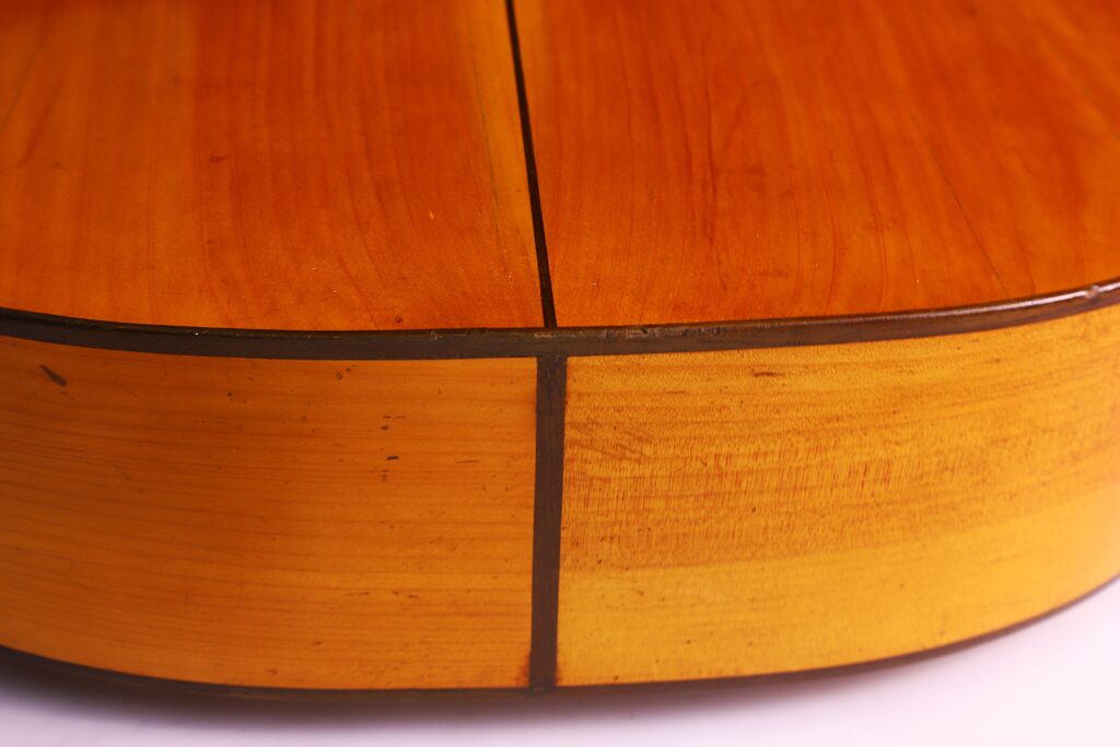 Grande plano do corpo de madeira da guitarra clássica Domingo Esteso 1934, destacando o seu acabamento brilhante, o grão da madeira visível e as linhas escuras das juntas.