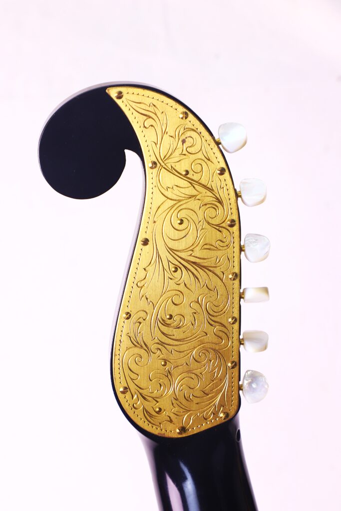 A Close-Up Of The Bernhard Kresse 2011 Stauffer Romantic Guitar'S Headstock Showcases An Ornate Gold Plate With Detailed Floral Engravings And Five White Tuning Pegs Against A Light Background.