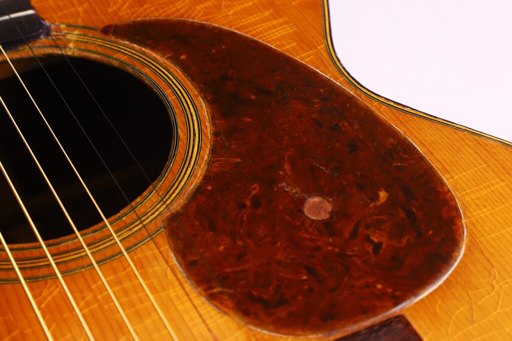 Close-Up Of The Martin 000-21 1947 Acoustic Guitar, Highlighting Its Strings, Sound Hole, And Marbled Brown Pickguard On A Wood-Textured Body.