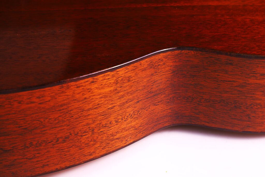 Close-Up View Of The Polished Wooden Side And Body Of A Martin 00-18 1946 Acoustic Guitar, With Warm Lighting Highlighting The Rich Brown Color And Fine Wood Grain Texture.