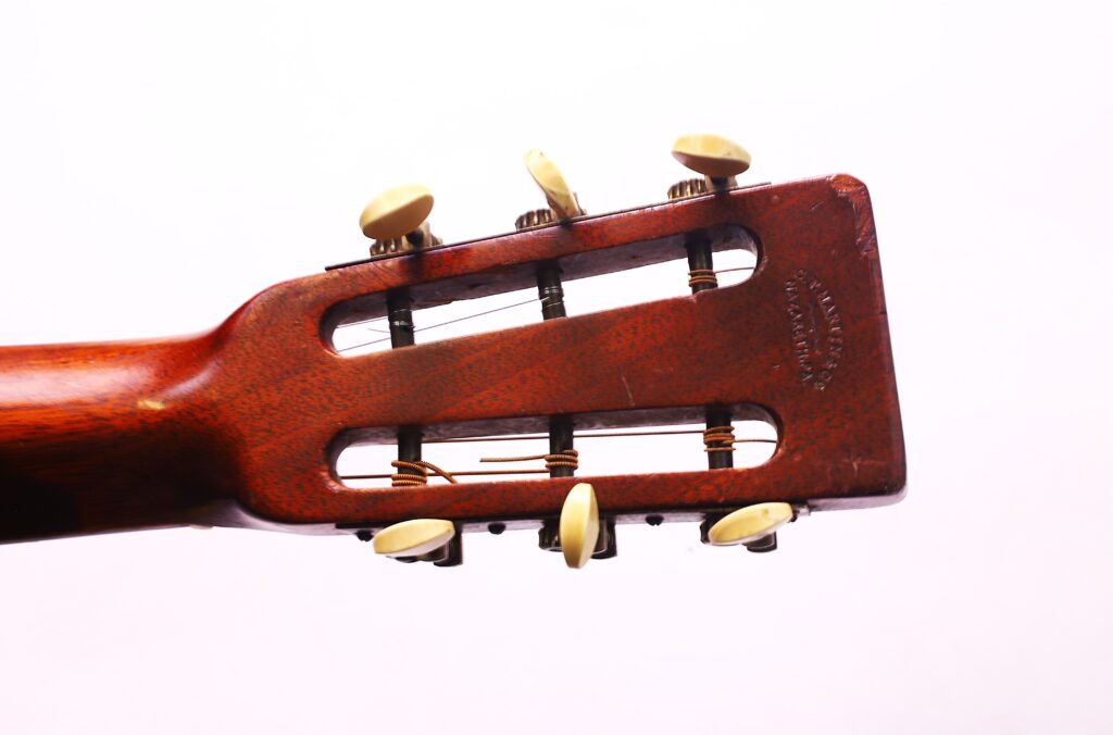 Close-Up Of The Martin 0-18 1926 Acoustic Guitar’s Headstock, Showing Six Tuning Pegs And String Ends, Against A Plain White Background.