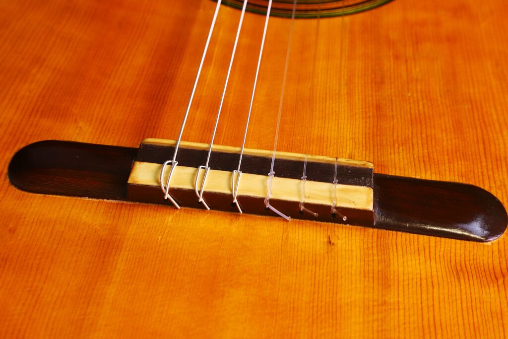 Grande plano do cavalete de uma guitarra clássica Domingo Esteso 1934, mostrando seis cordas presas ao seu corpo de madeira polida.