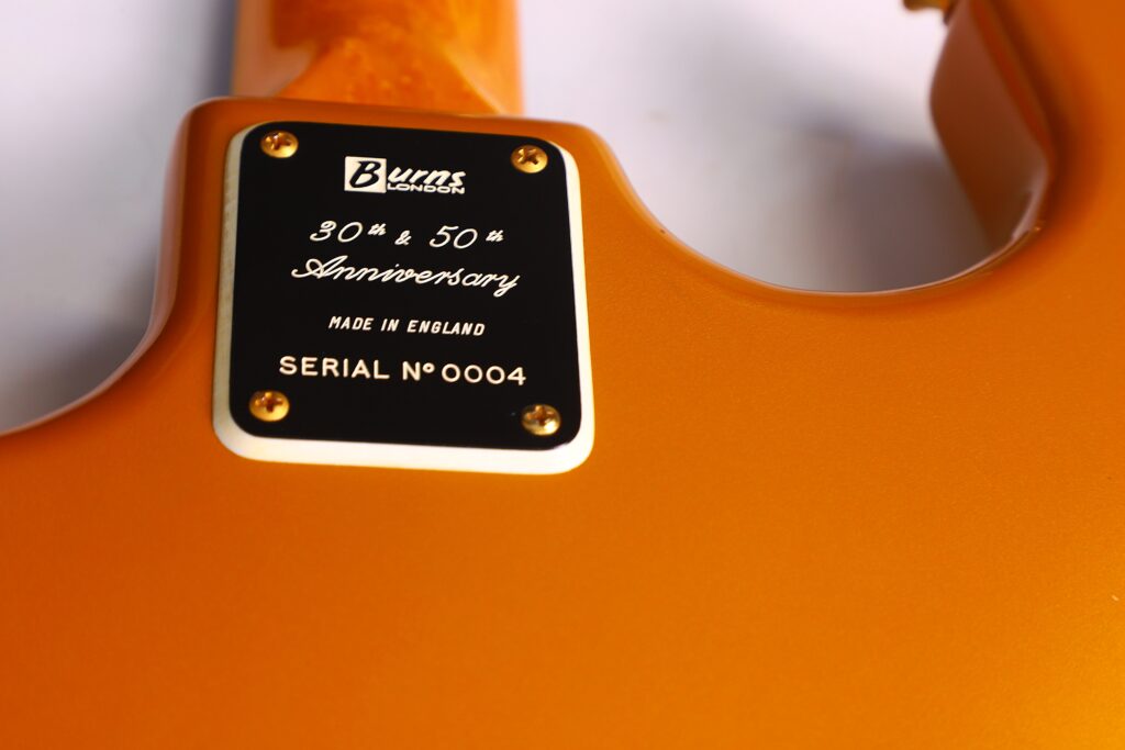 Close-Up Of A Gold-Colored Backplate On The Burns Legend 1994 Electric Guitar, Engraved With &Quot;Burns London, 30Th &Amp; 50Th Anniversary, Made In England, Serial No 0004,&Quot; And Attached With Four Screws.