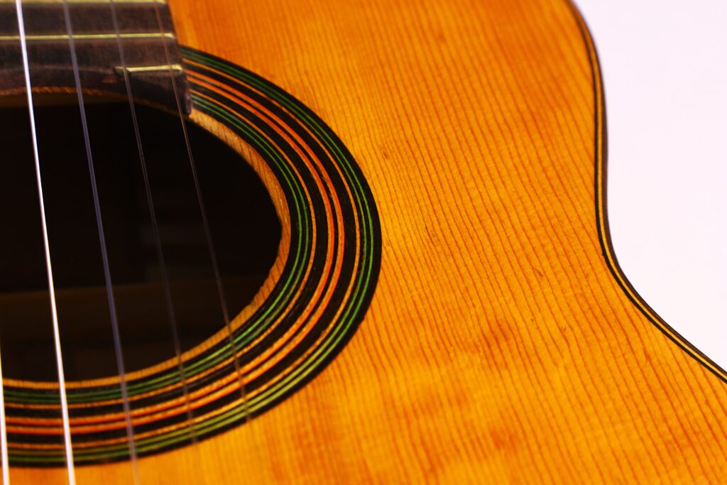 Grande plano da guitarra clássica Domingo Esteso 1934, destacando parte da caixa de ressonância, roseta e cordas, com o grão e a textura do corpo visíveis contra um fundo branco.