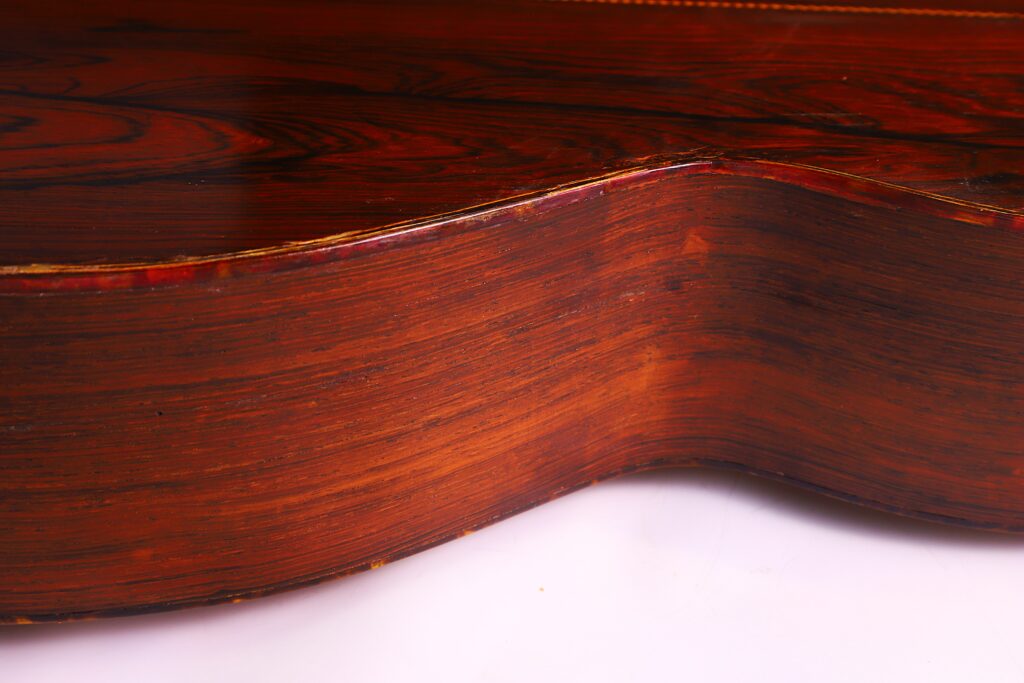 Close-Up View Of The Wood Grain And Curved Side Of A Martin 000-21 1947 Acoustic Guitar, Featuring Its Polished Brown Finish And Smooth Texture Against A White Background.