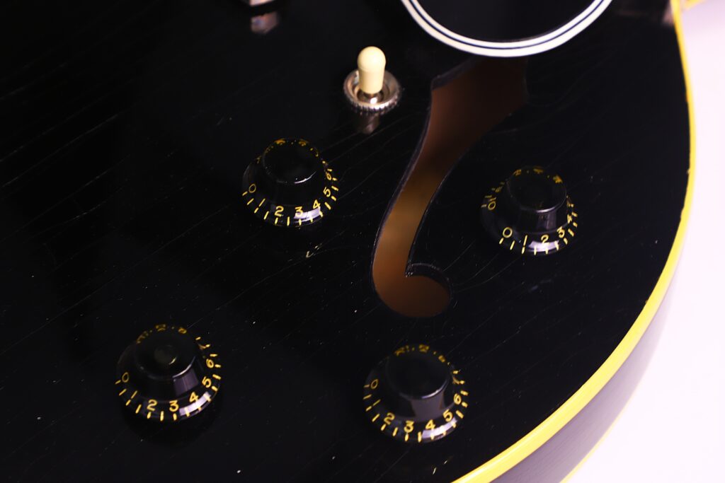 Nahaufnahme Des Schwarzen Korpus Einer Gibson Es-335 Td Murphy Lab E-Gitarre, Mit Vier Reglern Mit Gelben Ziffern, Einem Cremefarbenen Kippschalter Und Einem Mit Gelber Zierleiste Umrandeten F-Loch.