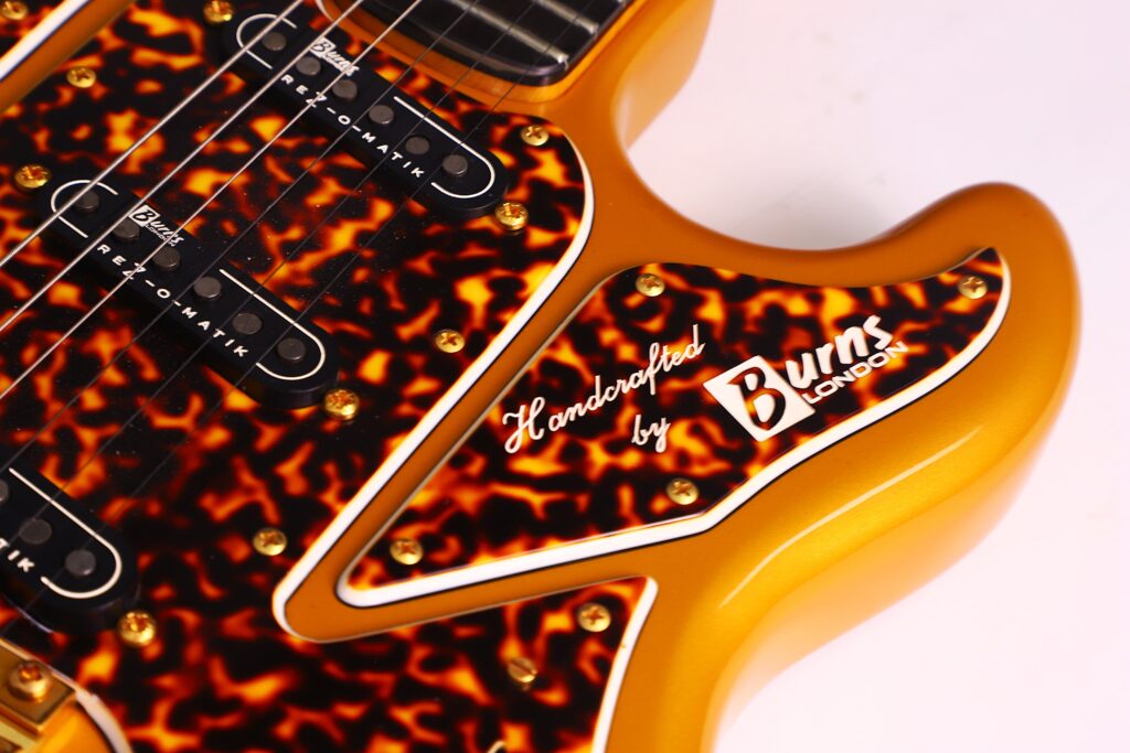 Close-Up Of A Burns Legend 1994 Electric Guitar In Gold With A Tortoiseshell Pickguard, Gold Screws, And White Trim. The Pickguard Is Inscribed With &Quot;Handcrafted By Burns London.