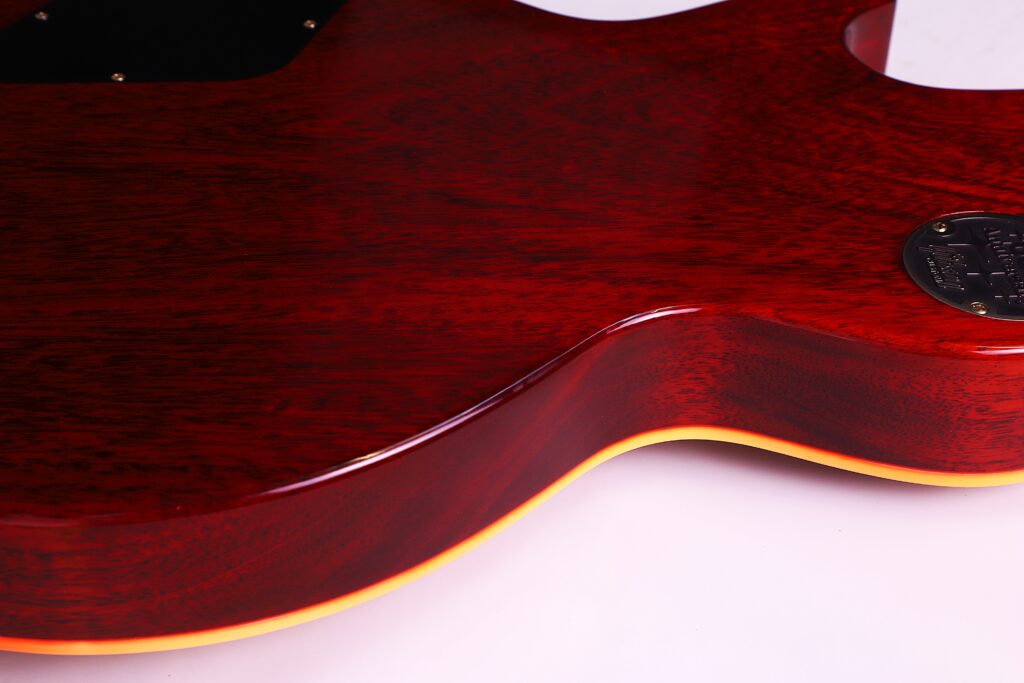Close-Up Of The Back Of A Gibson Les Paul 1960 60Th Vos Anniversary Electric Guitar, Highlighting Its Glossy Red Finish, Yellowish Edge Binding, And A Metal Plate With Engraved Text.