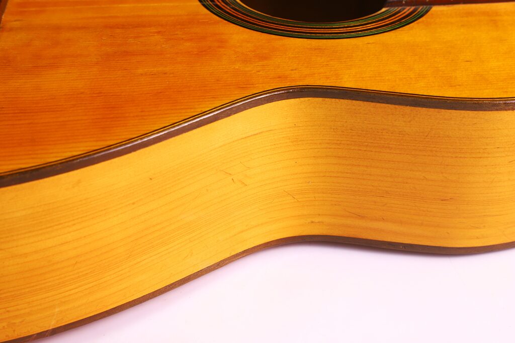 Grande plano da lateral e do corpo de uma guitarra clássica Domingo Esteso 1934, destacando o grão da madeira e as curvas elegantes contra um fundo branco.