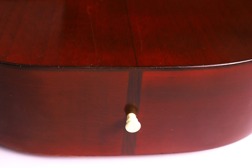 Close-Up Of The Bottom Edge Of A Martin 0-18 1926 Acoustic Guitar, Showing Its Glossy Reddish-Brown Finish And A White Strap Button Centered On The Lower Bout.