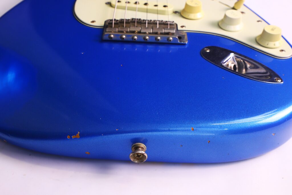 Nahaufnahme Des Unteren Korpus Einer Blauen Fender Stratocaster 1960 Relic Cunetto/Cruz E-Gitarre, Die Regler, Eingangsbuche Und Einen Teil Der Brücke Mit Kleineren Absplitterungen Und Kratzern Zeigt, Platziert Vor Einem Weißen Hintergrund.