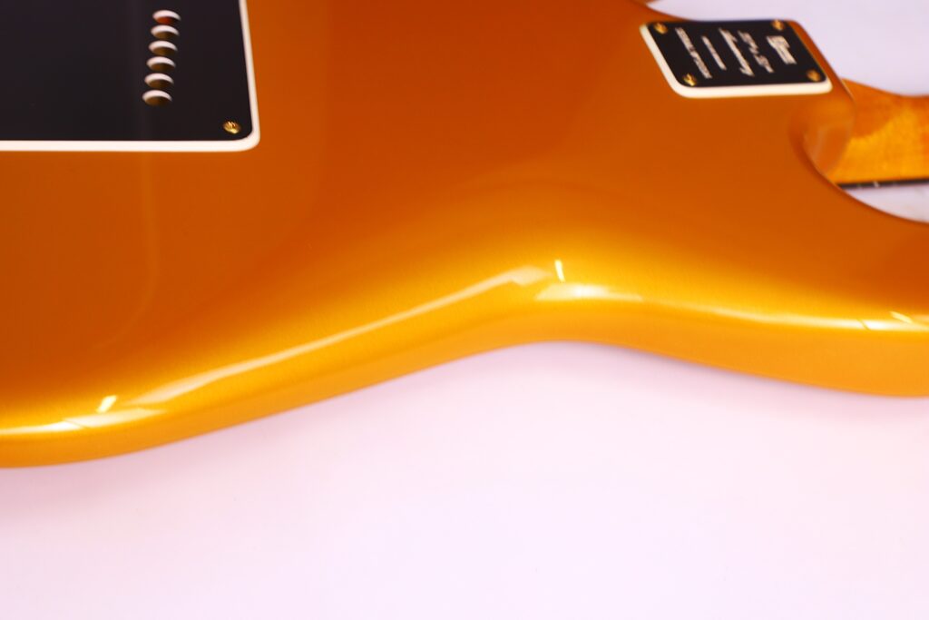 Close-Up Of The Glossy Gold Back Of A Burns Legend 1994 Electric Guitar, Featuring Part Of The Body And A Black Plate, Set Against A Pale Pink Background.