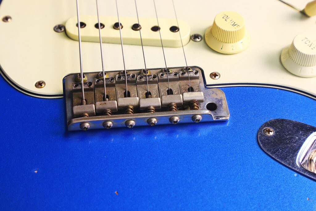 Nahaufnahme Der Brücke Und Der Regler An Einer Blauen Fender Stratocaster 1960 Relic Cunetto/Cruz E-Gitarre, Die Metallsaiten, Saitenreiter Und Einen Teil Des Schlagbretts Zeigt.