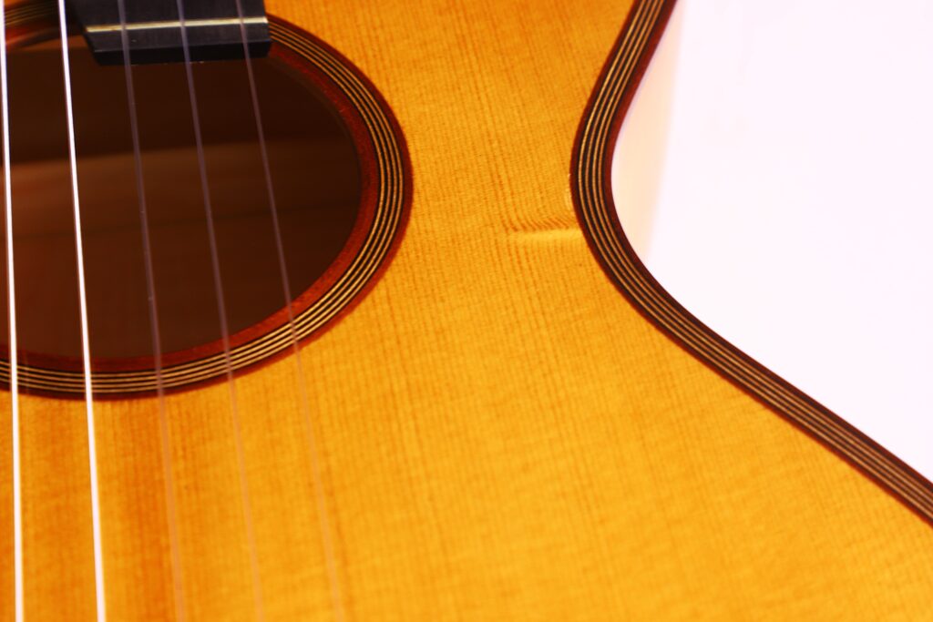 Close-Up Of A Bernhard Kresse 2011 Stauffer Romantic Guitar, Highlighting The Wood Grain, Strings, Part Of The Sound Hole, And The Guitar'S Edge Under Warm Lighting.
