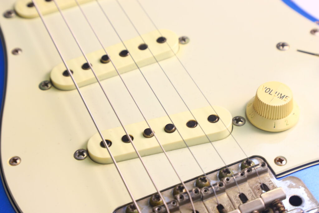 Nahaufnahme Einer Fender Stratocaster 1960 Relic Cunetto/Cruz E-Gitarre, Die Drei Single-Coil-Tonabnehmer, Saiten, Ein Cremefarbenes Schlagbrett, Einen Gelben „Volume“-Regler, Die Brücke Und Einen Teil Ihres Blauen Korpus Zeigt.