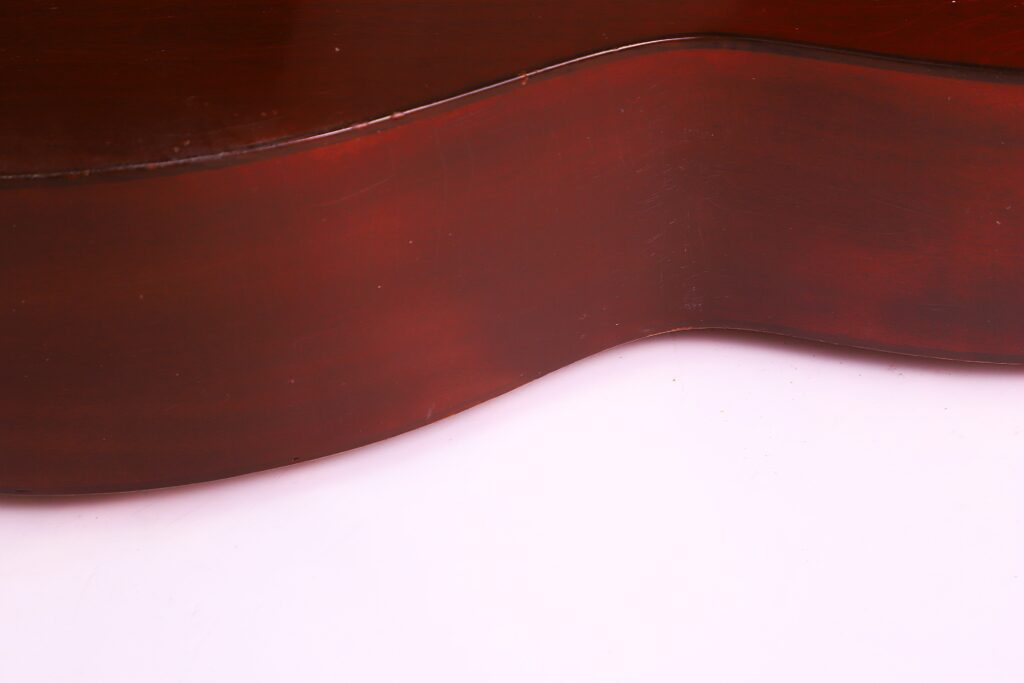 Close-Up Of The Martin 0-18 1926 Acoustic Guitar Side Against A Light Pink Background, Showcasing The Elegant Body Curve And Polished Reddish-Brown Finish.