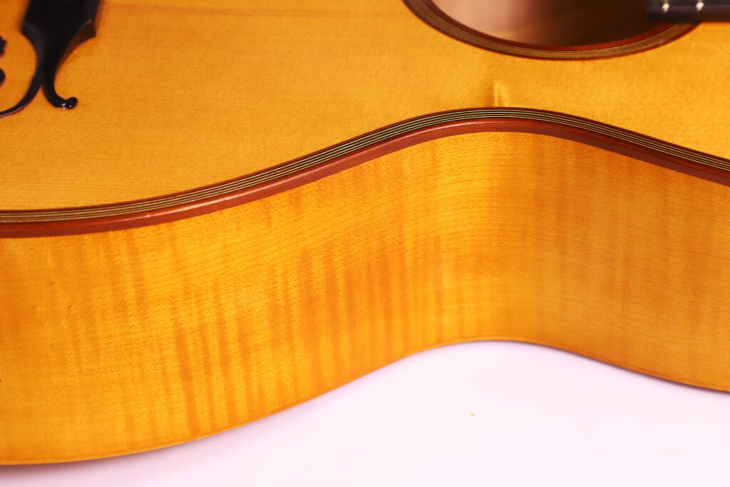 Close-Up Of The Side And Top Edge Of A Bernhard Kresse 2011 Stauffer Romantic Guitar, Highlighting Its Glossy, Golden-Brown Finish And Fine Wood Grain.