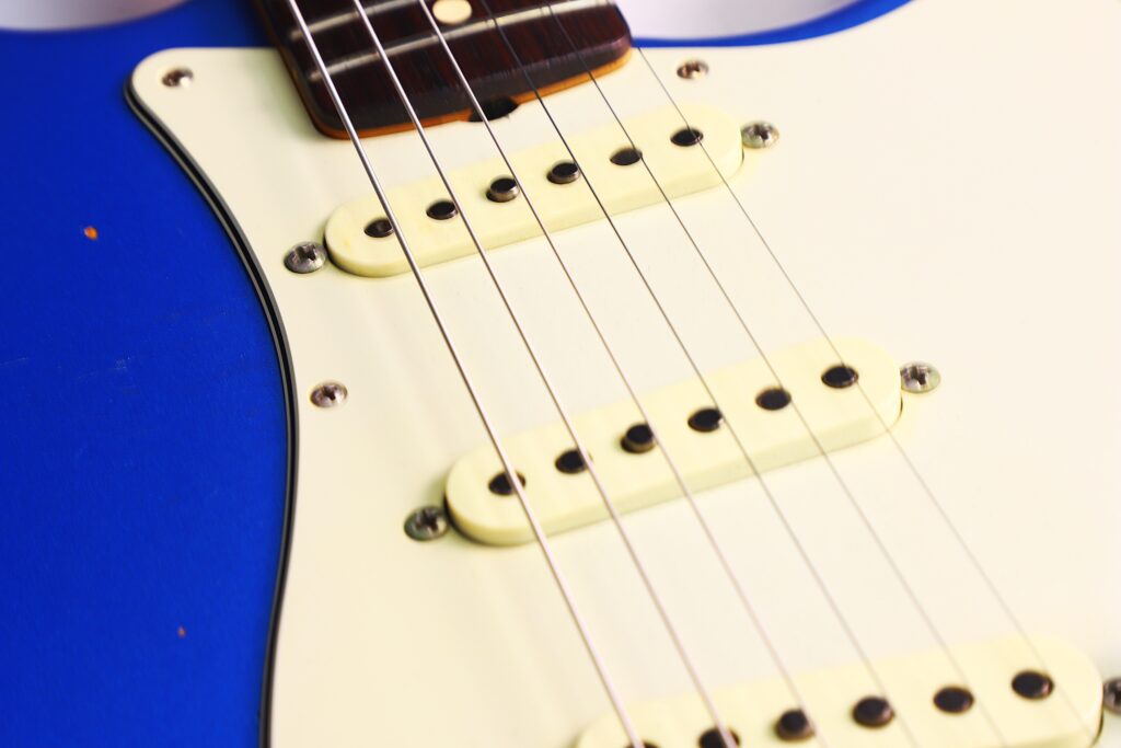 Nahaufnahme Einer Fender Stratocaster 1960 Relic Cunetto/Cruz E-Gitarre, Die Cremefarbene Tonabnehmer, Ein Weißes Schlagbrett Und Einen Teil Des Blauen Korpus Mit Stahlseiten Im Fokus Zeigt.