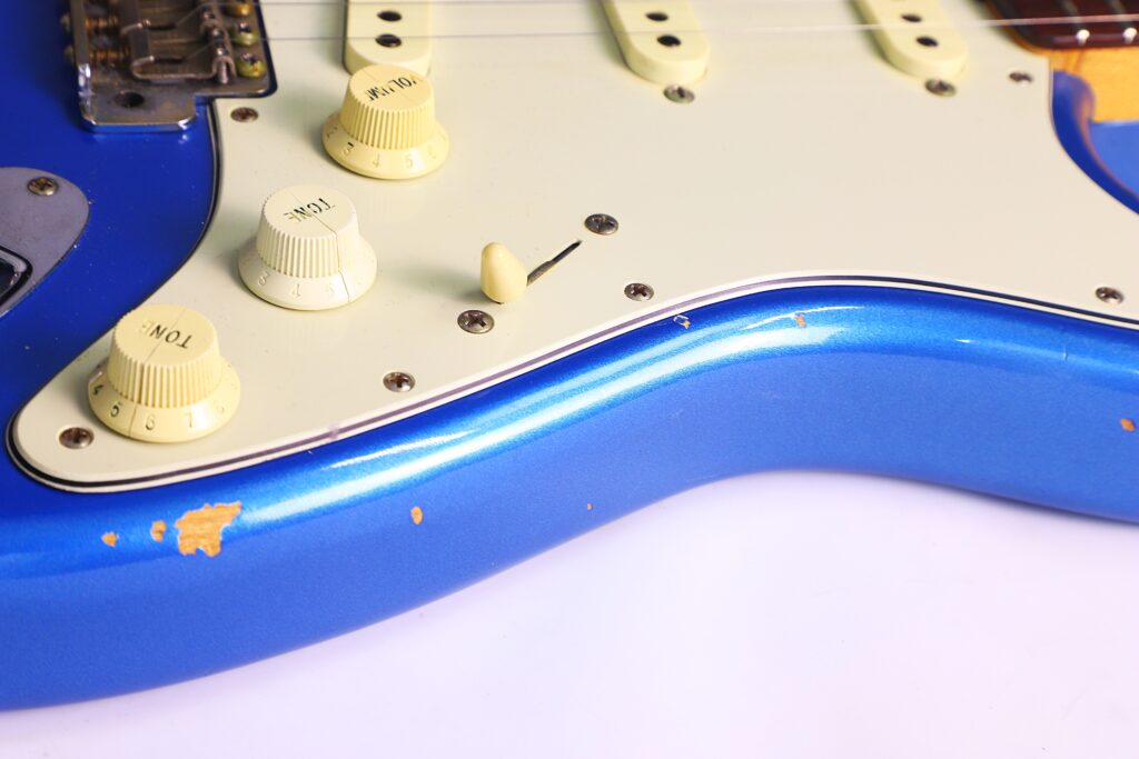 Nahaufnahme Einer Blauen Fender Stratocaster 1960 Relic Cunetto/Cruz E-Gitarre Mit Cremefarbenen Reglern, Einem Weißen Schlagbrett Und Abgesplitterter Farbe, Die Das Darunterliegende Holz Freilegt.
