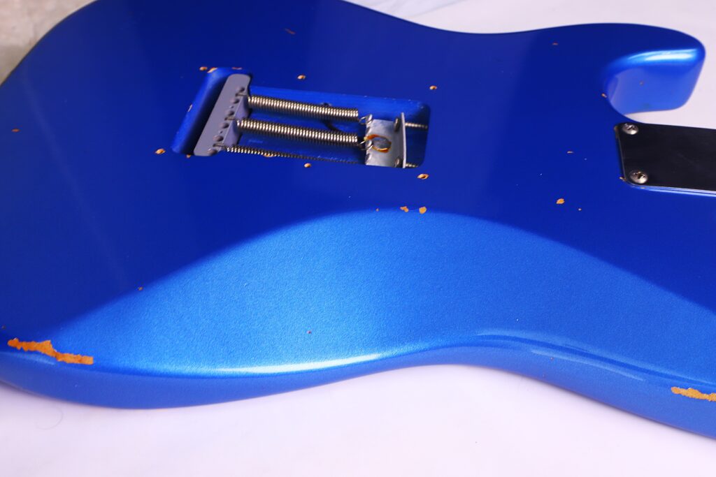 Eine Nahaufnahme Der Rückseite Einer Fender Stratocaster 1960 Relic Cunetto/Cruz E-Gitarre, Die Sichtbare Kratzer, Absplitterungen Und Abgenutzte Farbstellen Zeigt, Insbesondere Entlang Der Kanten Und Nahe Der Federkammer.