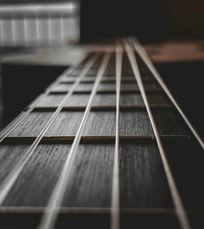 Close-up view of guitar strings and fretboard, with the focus on the strings and a blurred background, creating a dramatic and artistic perspective.