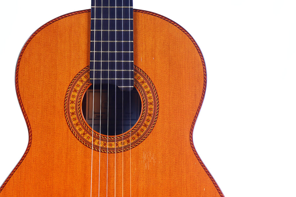 Nahaufnahme Des Oberen Korpus Und Der Saiten Einer Hopf La Portentosa 2004 Klassische Gitarre Vor Weißem Hintergrund, Wobei Die Detaillierte Rosette Um Das Schallloch Hervorgehoben Wird.