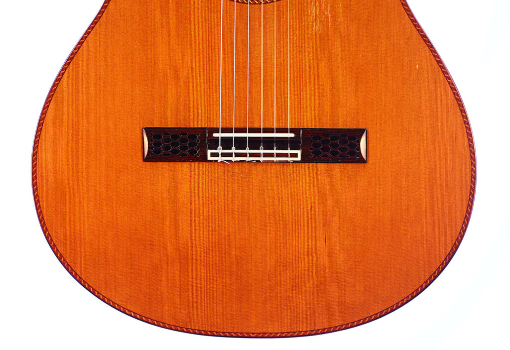 Nahaufnahme Der Unteren Hälfte Einer Hopf La Portentosa 2004 Klassische Gitarre, Die Den Hölzernen Korpus, Den Steg Und Die Sechs Saiten Vor Einem Weißen Hintergrund Zeigt.