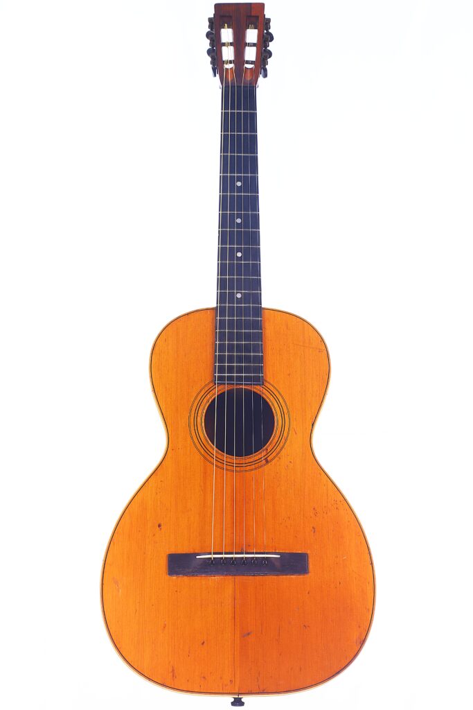 Die Washburn 1894 Parlor Akustik Gitarre Ist Eine Klassische Akustikgitarre Mit Einem Hellbraunen Holzkorpus, Einem Dunklen Griffbrett, Sechs Saiten Und Einem Runden Schallloch, Das Vor Einem Schlichten Weißen Hintergrund Steht.