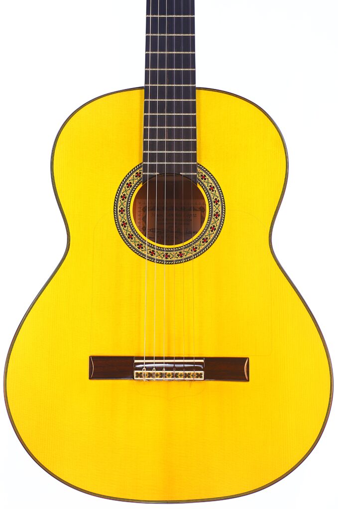 Die Hermanos Sanchis Lopez F Especial 2025 Mod. Reyes Flamenco-Gitarre Hat Einen Gelblichen Holzkorpus, Ein Dunkles Griffbrett Und Eine Verschnörkelte Rosette Um Das Schallloch, Die Auf Einem Weißen Hintergrund Dargestellt Ist.