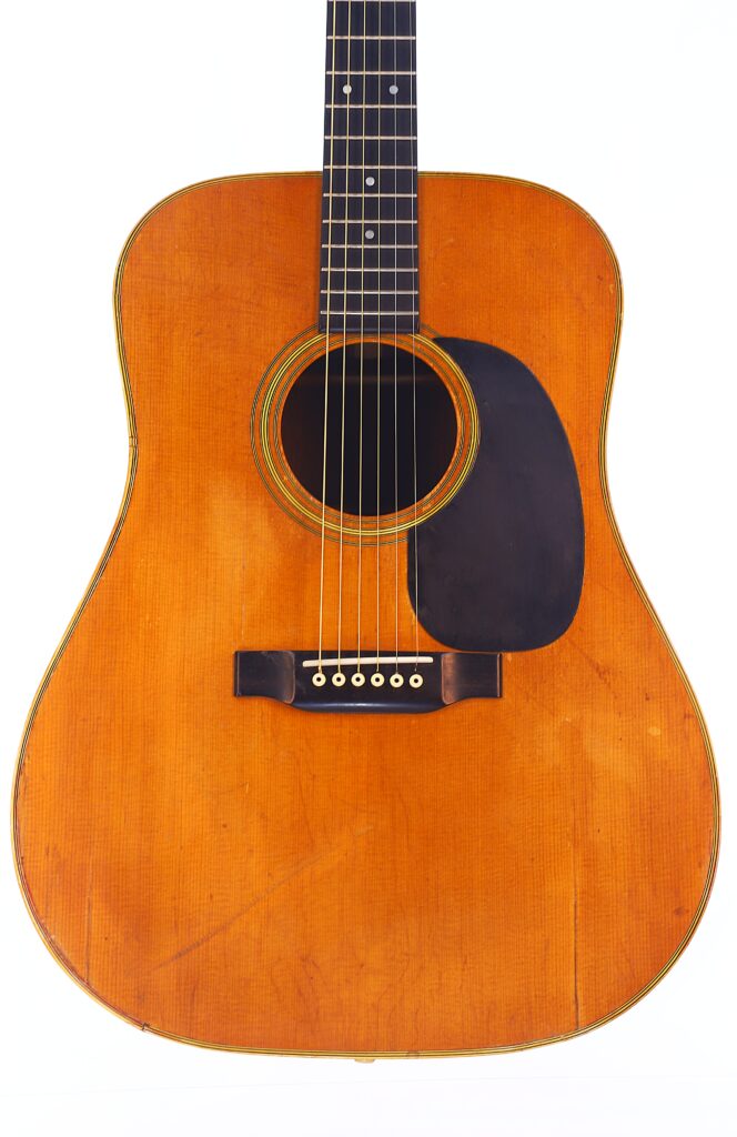 Eine Nahaufnahme Einer Martin D-28 1971 Akustik-Gitarre Mit Naturholz-Finish, Schwarzem Schlagbrett, Sechs Saiten Und Sichtbaren Gebrauchsspuren Und Kratzern Am Korpus.
